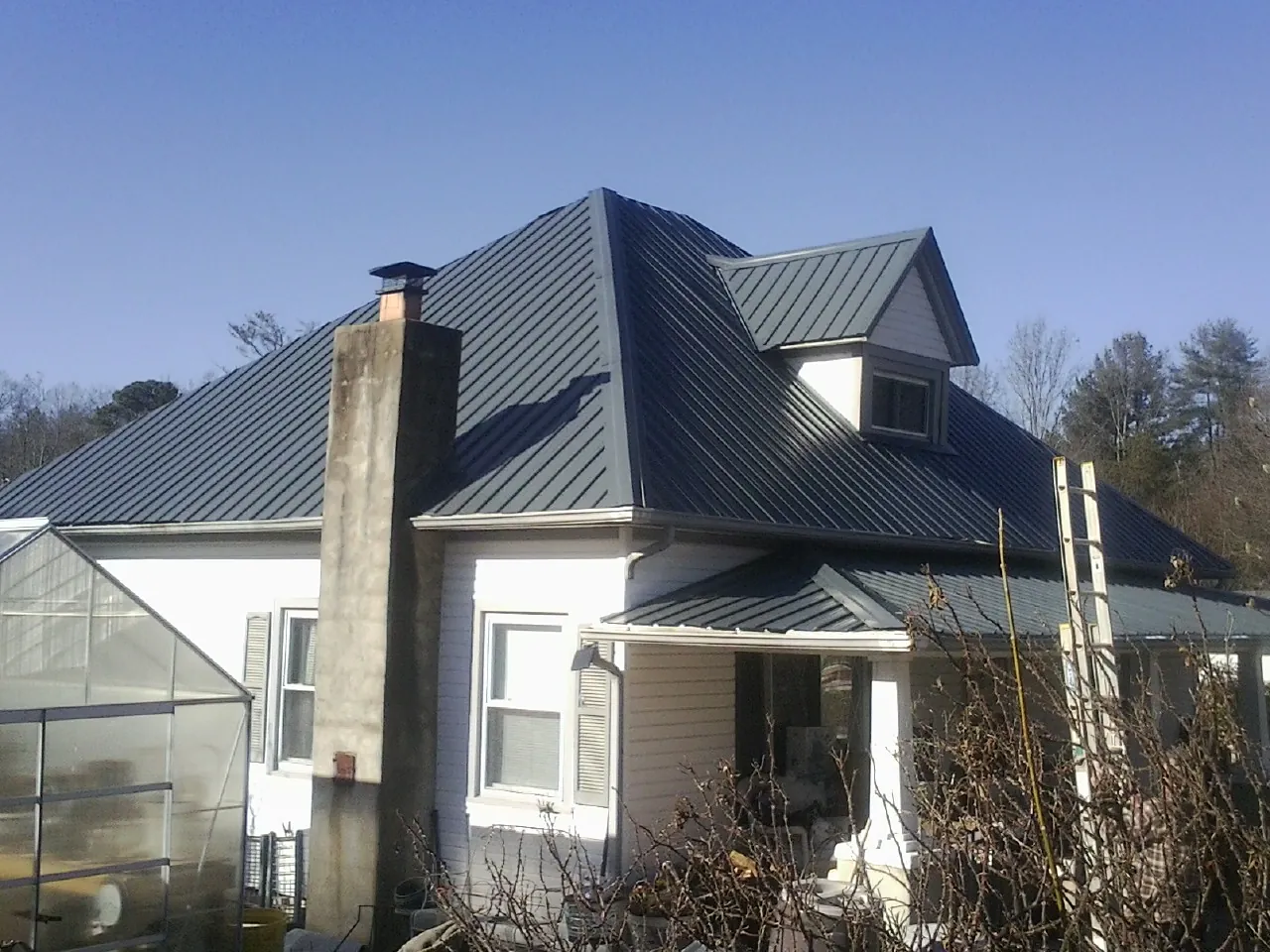 Dark blue standing seam metal roof on a white farmhouse with dormer — Slate & Tile Roof Repair by Roofing Brothers in Sugar Tree