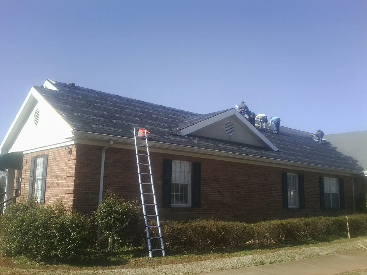 Crew tearing shingles off a brick ranch roof with a ladder set — Metal Roof Repair work by our crew in Sugar Tree