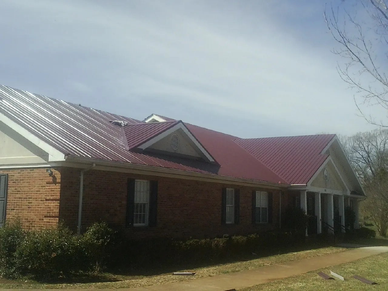 Red metal roof with gabled entries on a long brick building, from a Hail Damage Roof Repair job in Sugar Tree