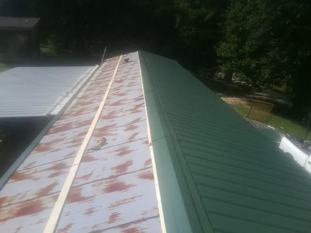 Old rusted panels beside newly installed green metal roofing — Wind Damage Roof Repair by Roofing Brothers in Sugar Tree