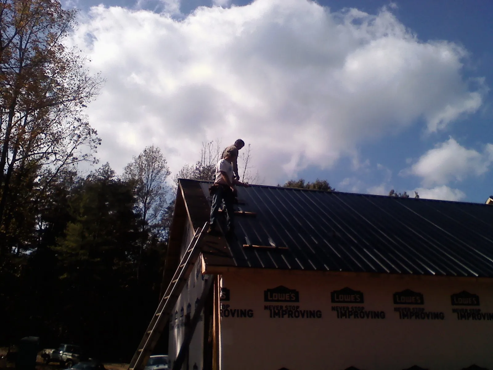 Roofer fastening dark metal panels high against a cloudy sky, from a Roof Inspection job in Sugar Tree