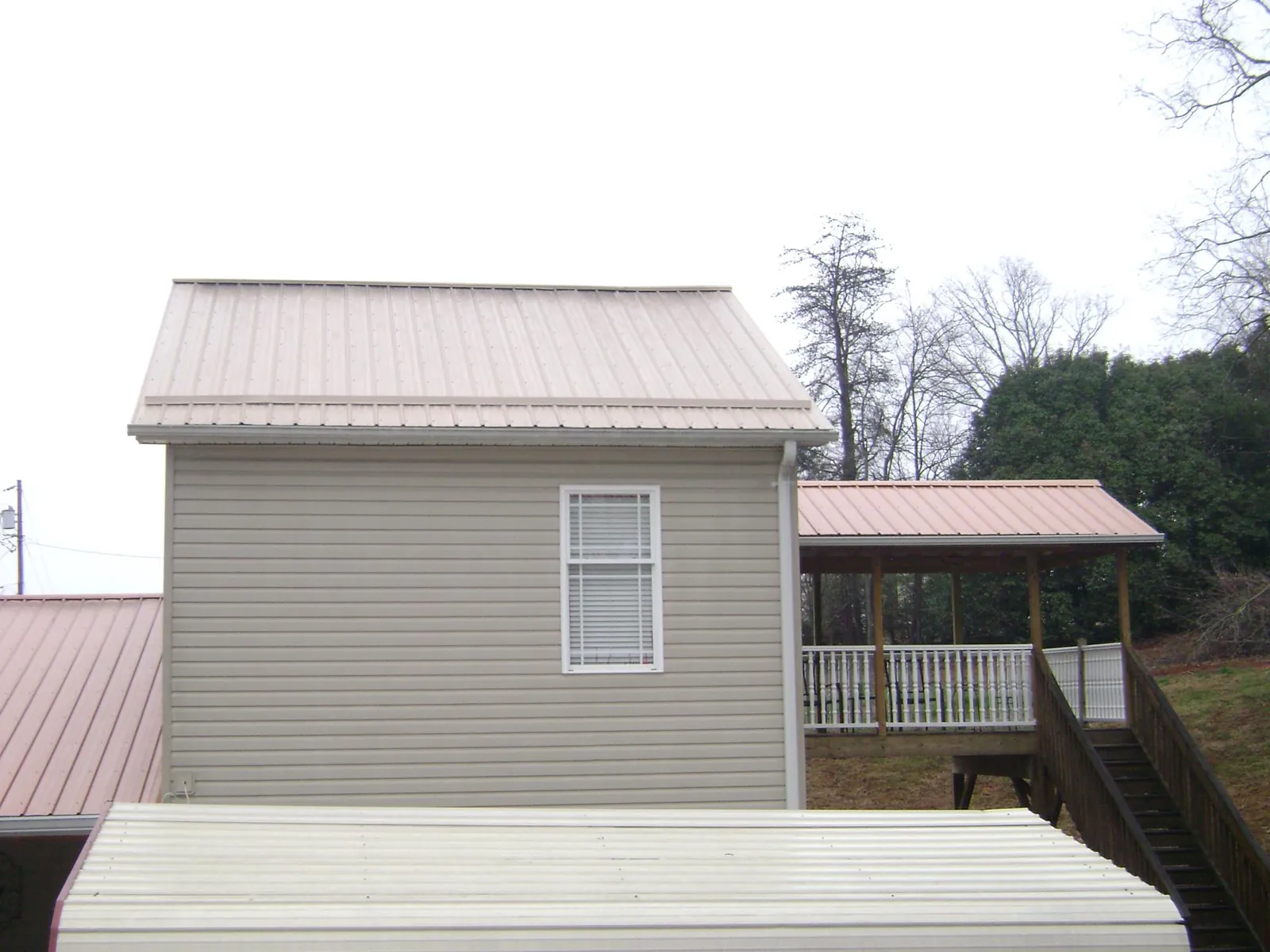 Tan metal roofs on a two story addition and attached porch, from a Roof Replacement job in Sugar Tree